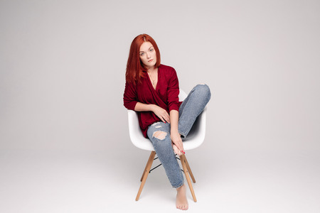 Model with ginger hair sitting on white chair in studio.の写真素材