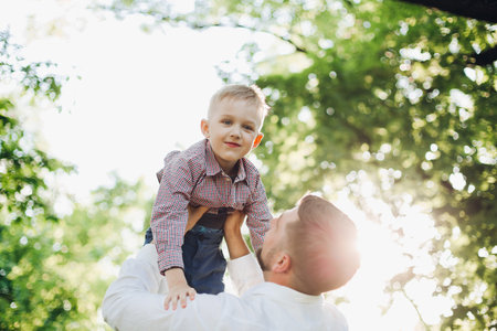 Handsome father throwing baby boy against summer park.の写真素材