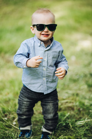 Portrait of stylish little boy posing in park in summertime.