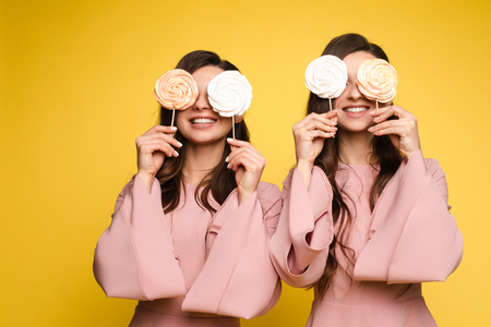 Charming twins closing eyes with lollipops and posingの写真素材