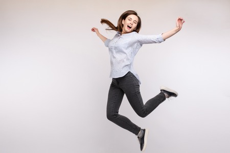 Cheerful brunette young woman in casual outlook jumping in mid air in studio.の写真素材