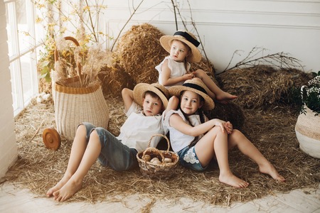 Cute sisters and brother in hay hats resting on hayの写真素材