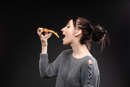 Young caucasian woman with tail eating piece of pizza.の写真素材