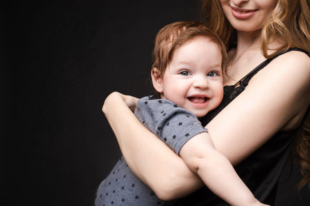 Adorable baby son sitting on mothers arms.