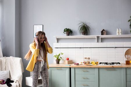 Stylish woman in yellow jacket and blue headphones singing.の写真素材