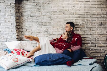 Couple in red Christmas jumpers kissing surrounded by pillows.の写真素材