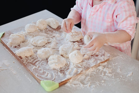 Little lovely kid helping parent with dough at kitchen.