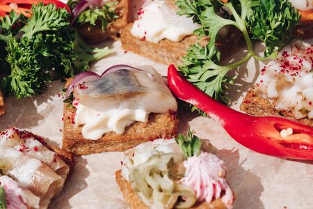 Delicious sandwiches with herring and onion.Close-up of tasty crispy sandwiches or canapes with cream cheese, onion and herring on the top. Parsley and chilli pepper on the platter.の写真素材
