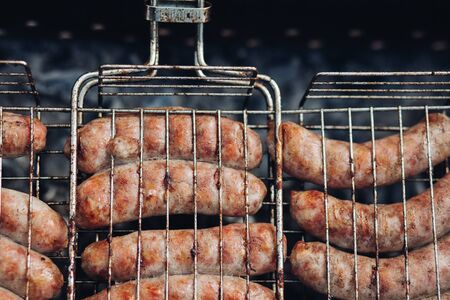 Sausages on grill at bbq party.Close-up of delicious chicken or pork sausages on BBQ. Unrecognizable cook preparing tasty sausages on grill.の写真素材