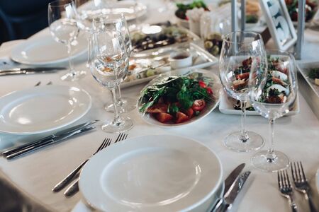 View over wedding table covered with white tablecloth with empty glasses, plates and utensils. Snacks are served on the table.の写真素材