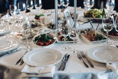 View over wedding table covered with white tablecloth with empty glasses, plates and utensils. Snacks are served on the table.の写真素材