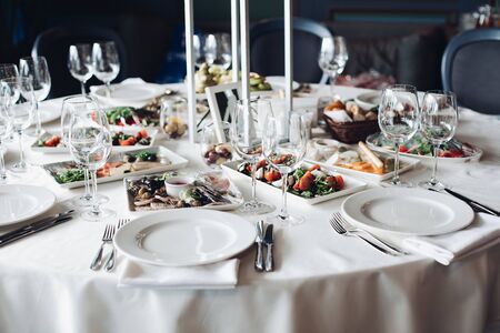 View over wedding table covered with white tablecloth with empty glasses, plates and utensils. Snacks are served on the table.の写真素材