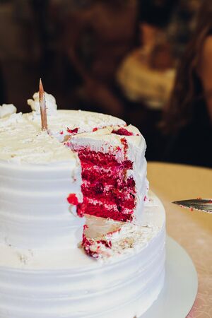 Close-up tasty big appetizing fresh piece of layered biscuit cake covered by white whipped cream icing. Beautiful dessert food serving for banquet event people guest at background. red velvetの写真素材