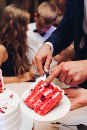 Close-up tasty big appetizing fresh piece of layered biscuit cake covered by white whipped cream icing. Beautiful dessert food serving for banquet event people guest at background. red velvetの写真素材