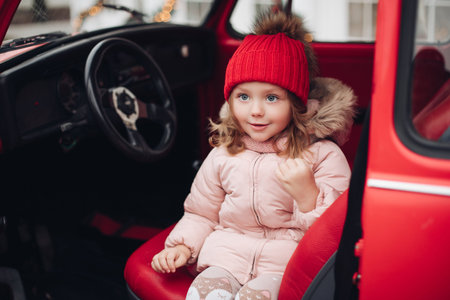 Smiling cute winter girl in red hat sitting in car having fun