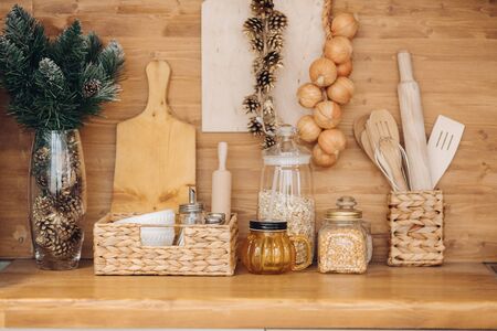 Close-up of kitchen table over wooden background with vase of fir tree and pine cones, containers of cereals, onions and kitchenware.の写真素材