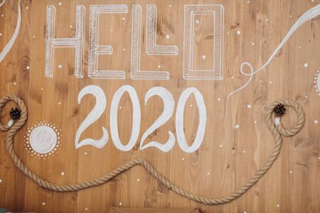 Wooden background with painted white numbers 2020 and word HELLO from above. Top view of upcoming New Year numbers with rope and pine cones.の写真素材