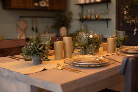 Close-up of beautifully decorated dining table with fir trees in vases and gold candles. Sets of...