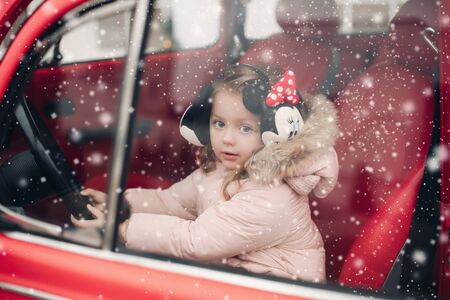 Lovely little girl in earmuffs sitting in red car.の写真素材
