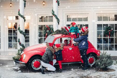 Parents and children with New Year presents and Christmas tree. Dad, mom, daughters and son are going for Christmas holidays by carの写真素材