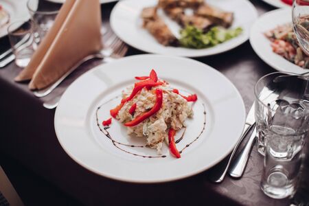 Wedding catering. White ceramic plate with tasty salad with red pepper on top in close-up.の写真素材