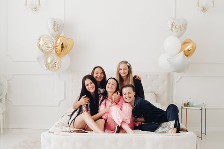 Group of happy girl friends laughing posing on bed enjoying pajamas party