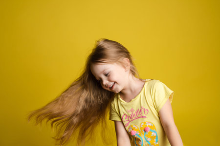 Portrait of beautiful little girl with long hair smiling posing isolated at yellow studio background