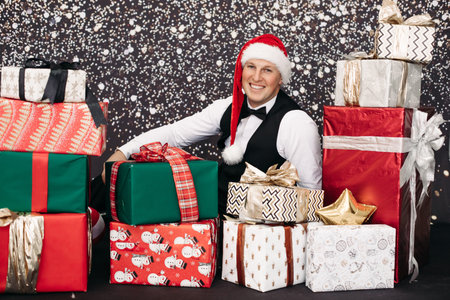 Smiling man in suit wearing Santa Claus hat posing with Christmas gift surrounded by snowの写真素材