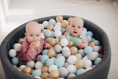 Two cute little toddler posing sitting in bucket with colorful balls having fun