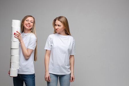 Portrait of two handsome girls with long fair hair, one of them holds a lot of toilet paper and other is offendedの写真素材