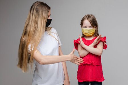 Portrait of two handsome girls with long fair hair with medical masks on their faces, prohibited shaking handsの写真素材