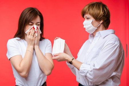 Beautiful woman is sick and sneezes in napkin near her mum, picture isolated on red backgroundの写真素材