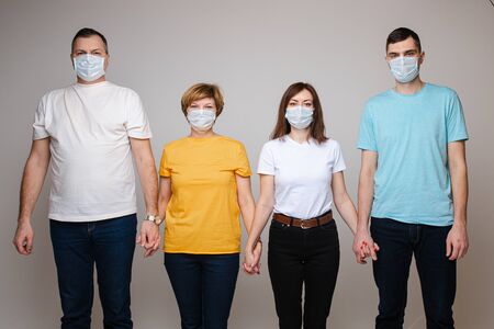 Group of people holding hands posing in medical safety mask isolated at white studioの写真素材