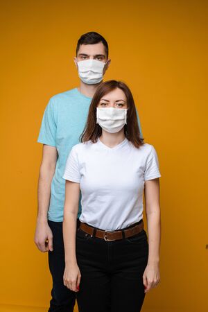 Couple in love in white medical masks are scared by coronavirus, picture isolated on yellow backgroundの写真素材