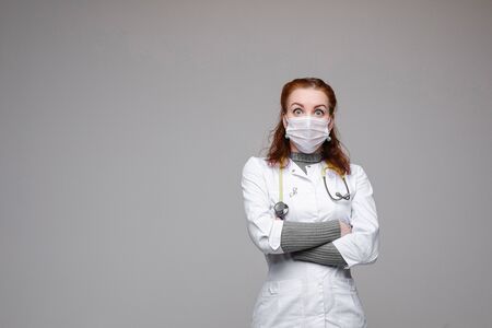 Doctor in white coat and mask looking shocked at camera.の写真素材