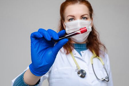 Handsome woman in white medical clothes, mask, blue gloves and phonendoscope on her shoulders, picture isolated on grey backgroundの写真素材