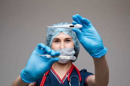Portrait of female doctor in medical clothes with phonendoscope around her neck holds thermometers, picture isolated on white backgroundの写真素材