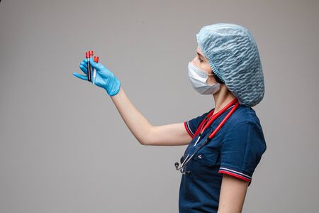 Portrait of female doctor in medical clothes with phonendoscope around her neck holds several test tubes, picture isolated on white backgroundの写真素材