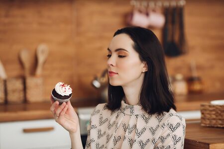 Handsome young woman made marshmallows and eats it in her big bright kitchen with pleasureの写真素材