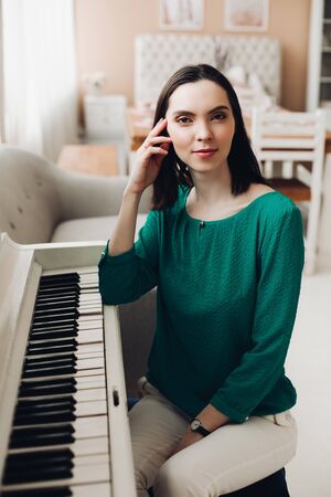 Cheerful lady sits on the chair near the white pianoの写真素材