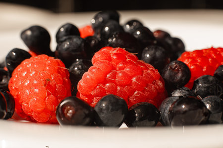 Many juicy fresh ripe red strawberry berries lie in a white ceramic plate on the table under bright...