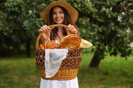 Portrait of a young beautiful girl with even white teeth, a beautiful smile in a straw hat have a picnic in the gardenの写真素材