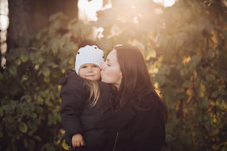 Loving mother kissing her daughter in autumnal forest.の写真素材