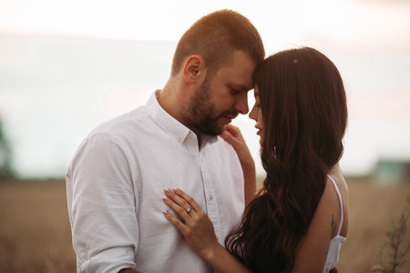 Pretty caucasian woman with long dark wavy hair in white dress hugs with beautiful man in white...