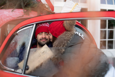 Young lovely couple buys Christmas presents for their family and take them to home in a red car