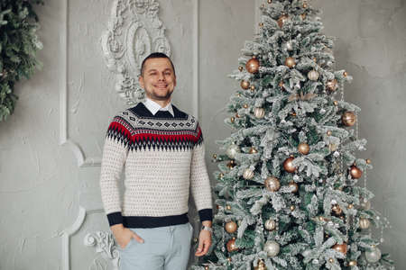 Joyous gentleman in warm sweater standing near Christmas treeの写真素材
