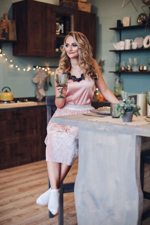 Blonde woman in pink with glass in kitchen.の写真素材