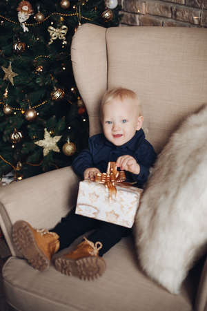 little caucasian boy sits near the christmas tree with a giftの写真素材