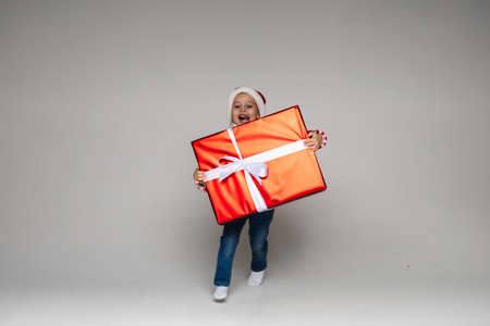 Cheerful kid carrying Christmas present.Cutout on grey background.の写真素材
