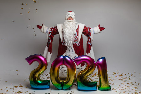 Xmas New Year 2021 celebration, gray-haired bearded Santa man with balloons with welcoming gesture...